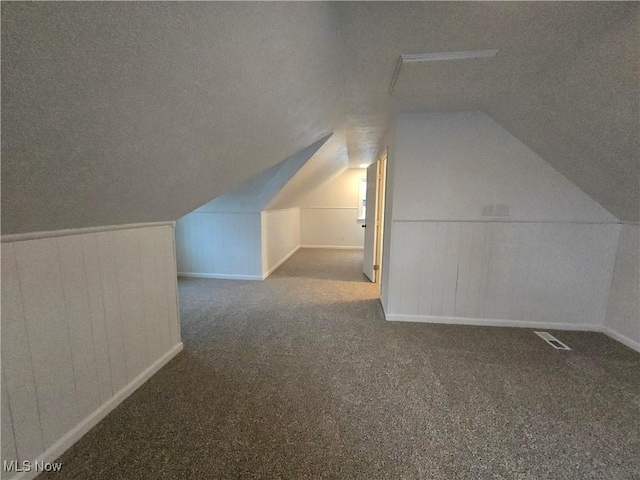 additional living space with a textured ceiling, carpet flooring, and vaulted ceiling