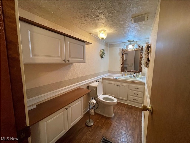 bathroom with hardwood / wood-style flooring, vanity, toilet, and a textured ceiling