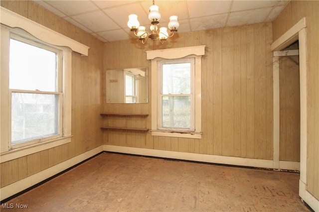 unfurnished room with wood walls, a notable chandelier, and a healthy amount of sunlight