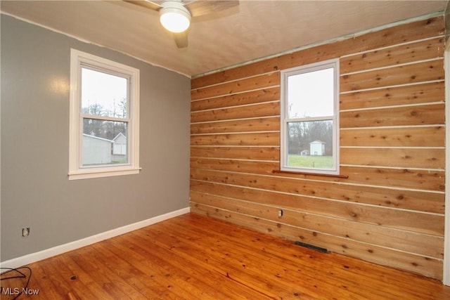 empty room featuring hardwood / wood-style floors, ceiling fan, and wooden walls