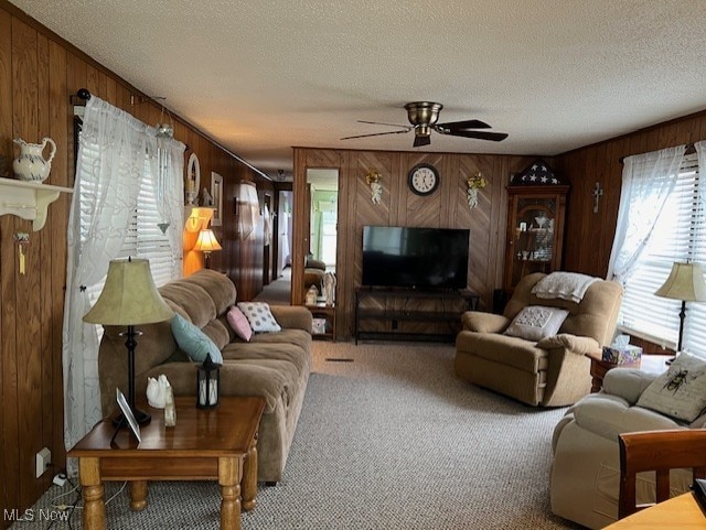 carpeted living room featuring ceiling fan, wood walls, and a textured ceiling