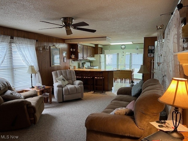 carpeted living room with a textured ceiling, ceiling fan, and wood walls