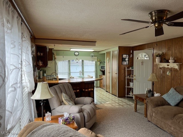 carpeted living room with wood walls, ceiling fan, and a textured ceiling