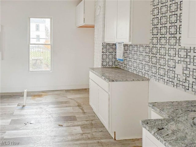 kitchen featuring light stone countertops, white cabinetry, light wood finished floors, and backsplash