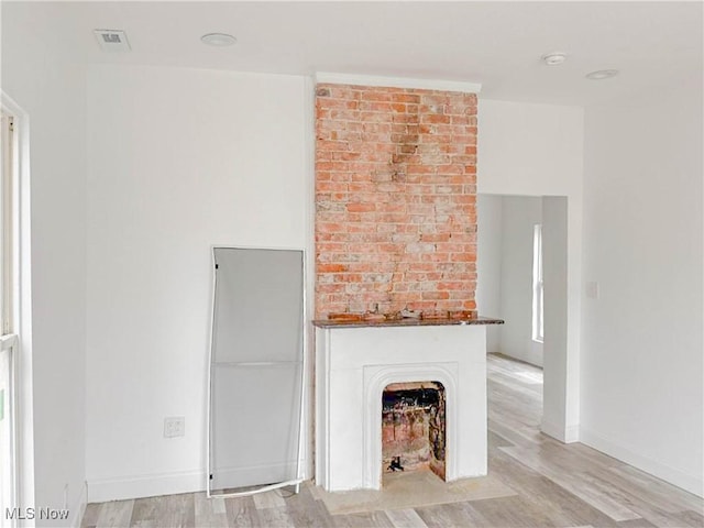 unfurnished living room with visible vents, a fireplace with flush hearth, light wood-style flooring, and baseboards