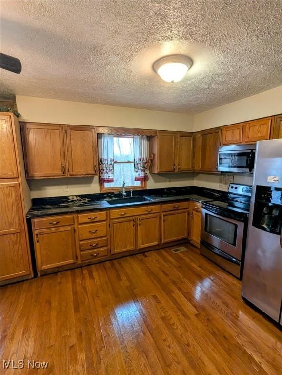 kitchen featuring sink, dark hardwood / wood-style flooring, a textured ceiling, and appliances with stainless steel finishes