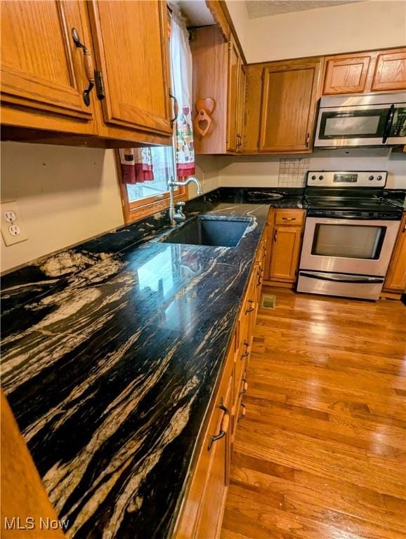 kitchen featuring sink, light wood-type flooring, stainless steel appliances, and dark stone counters