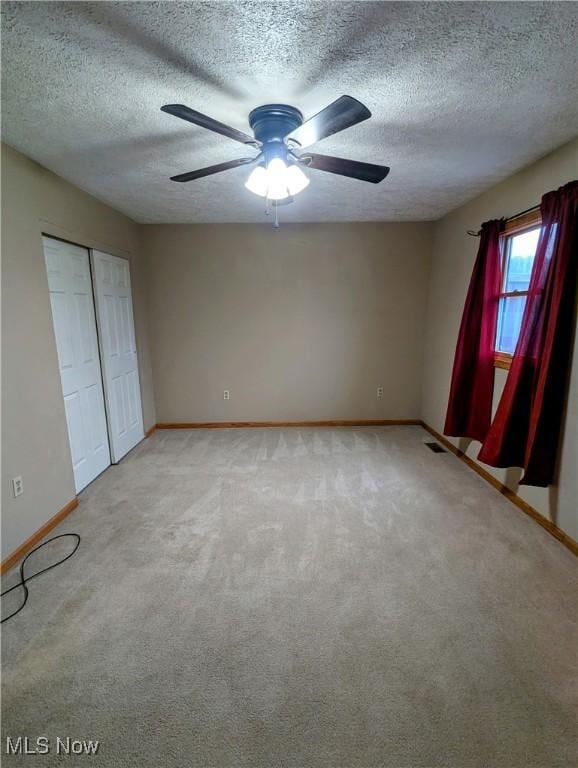 unfurnished bedroom featuring light carpet, a textured ceiling, a closet, and ceiling fan