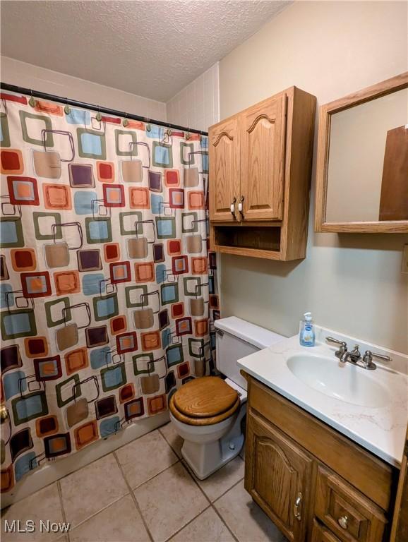 bathroom with curtained shower, tile patterned flooring, a textured ceiling, toilet, and vanity