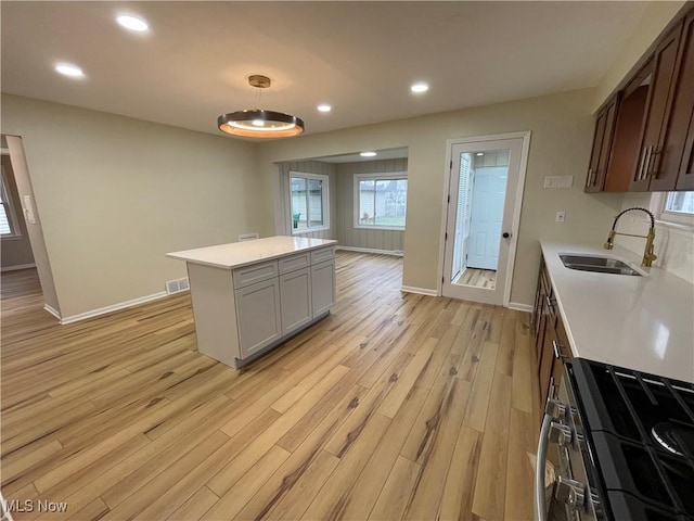 kitchen featuring dark brown cabinetry, sink, stainless steel gas range, light hardwood / wood-style floors, and a kitchen island