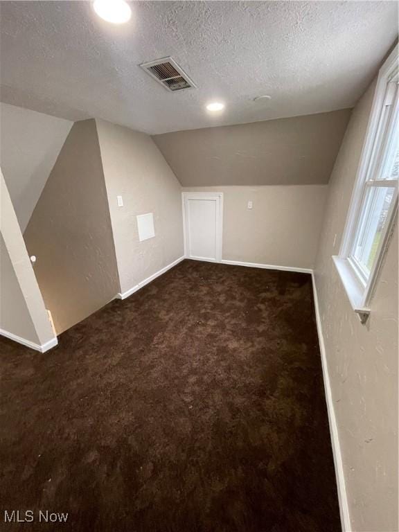 bonus room with a textured ceiling, vaulted ceiling, and dark colored carpet