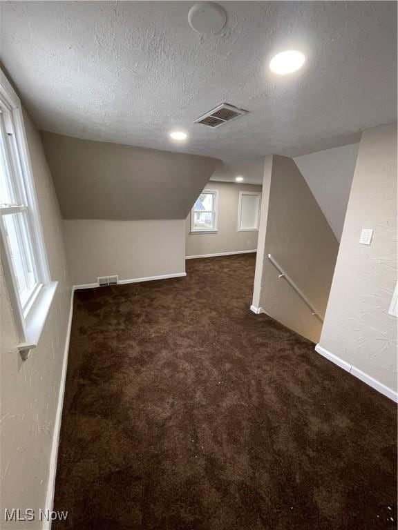 bonus room featuring a textured ceiling, vaulted ceiling, and dark colored carpet