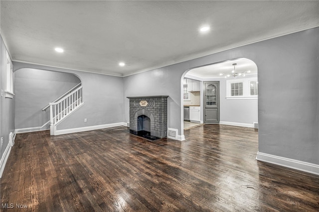 unfurnished living room featuring an inviting chandelier, dark wood-type flooring, and a brick fireplace