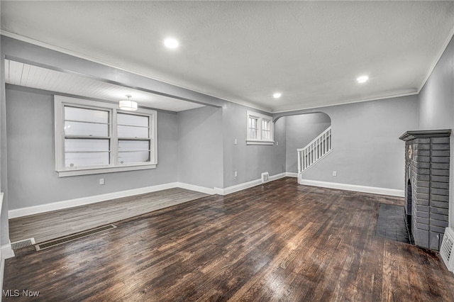 basement featuring a brick fireplace, ornamental molding, built in shelves, a textured ceiling, and dark hardwood / wood-style floors