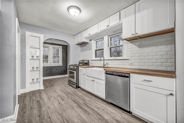 kitchen with sink, wood counters, appliances with stainless steel finishes, white cabinets, and light wood-type flooring