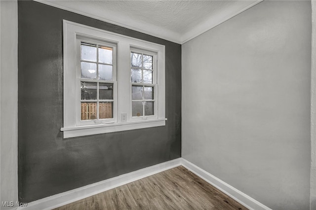 empty room with wood-type flooring, a textured ceiling, and crown molding