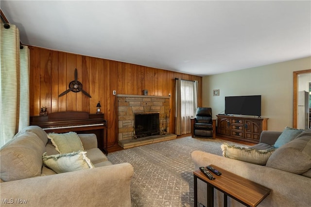 living room with ceiling fan, wood walls, and a stone fireplace