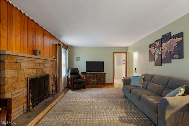 living room featuring a stone fireplace and wood walls