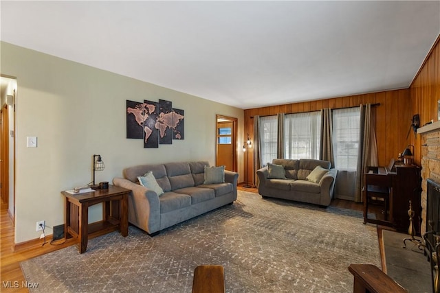 living room featuring a stone fireplace, wooden walls, and dark hardwood / wood-style floors