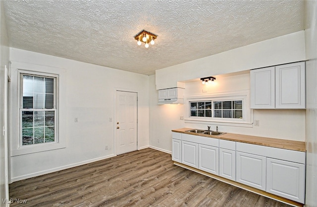 kitchen featuring butcher block counters, sink, wood-type flooring, a textured ceiling, and white cabinets