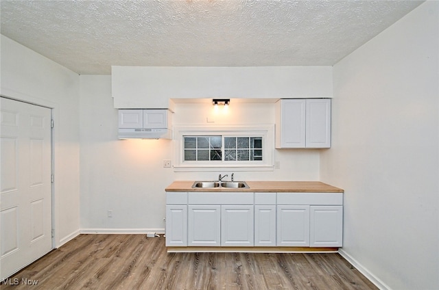 kitchen featuring a textured ceiling, butcher block counters, light wood-type flooring, and sink