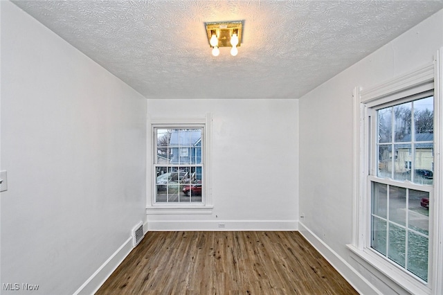 empty room featuring a textured ceiling, hardwood / wood-style flooring, and a healthy amount of sunlight