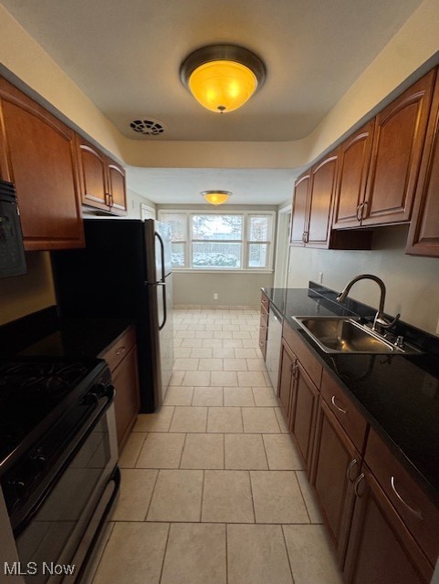 kitchen featuring dishwasher, black gas range, light tile patterned flooring, and sink