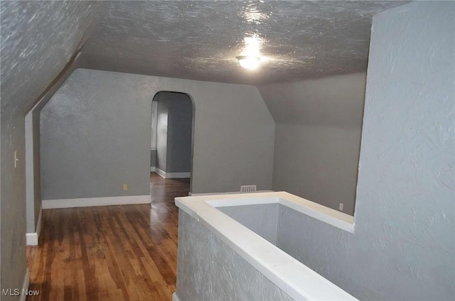 hallway featuring dark hardwood / wood-style flooring, lofted ceiling, and a textured ceiling