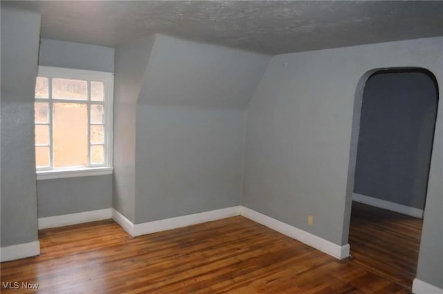 bonus room with wood-type flooring, a textured ceiling, and vaulted ceiling