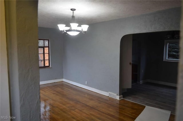 spare room with dark wood-type flooring, a textured ceiling, and an inviting chandelier