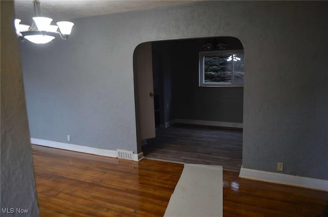 spare room featuring a textured ceiling, a notable chandelier, and dark wood-type flooring