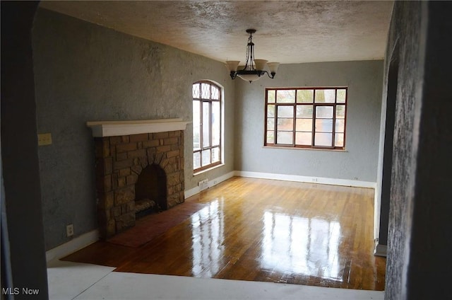 unfurnished living room featuring a stone fireplace, light hardwood / wood-style flooring, a healthy amount of sunlight, and a notable chandelier