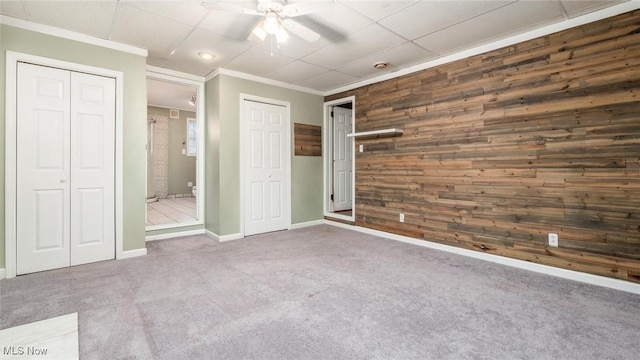 unfurnished bedroom with carpet floors, ceiling fan, ornamental molding, and wood walls