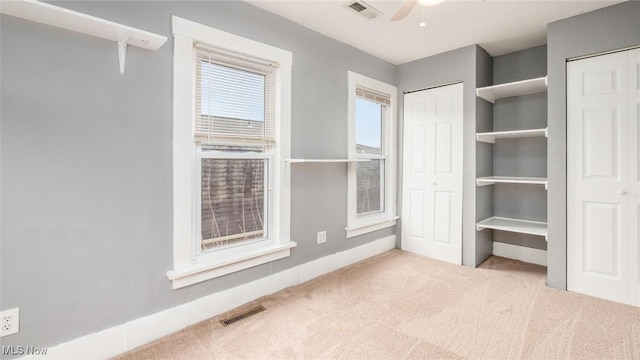 unfurnished bedroom featuring ceiling fan, light carpet, and two closets