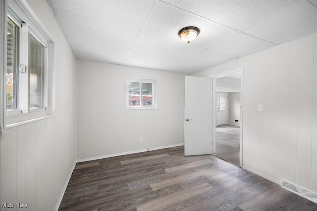 spare room with a paneled ceiling, wooden walls, and dark wood-type flooring