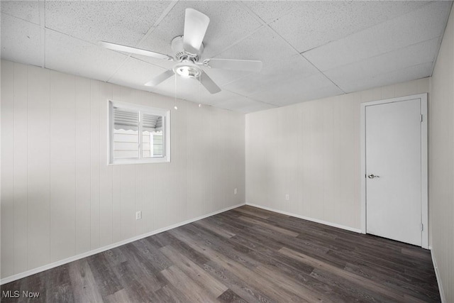 spare room featuring wooden walls, a drop ceiling, dark wood-type flooring, and ceiling fan