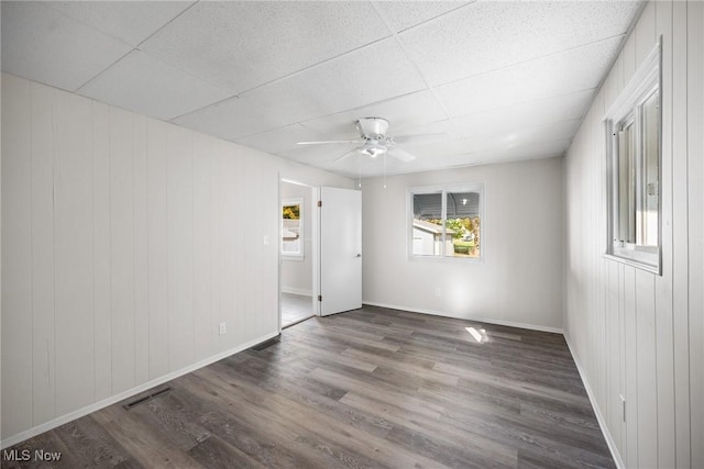 spare room with a paneled ceiling, ceiling fan, hardwood / wood-style floors, and wooden walls