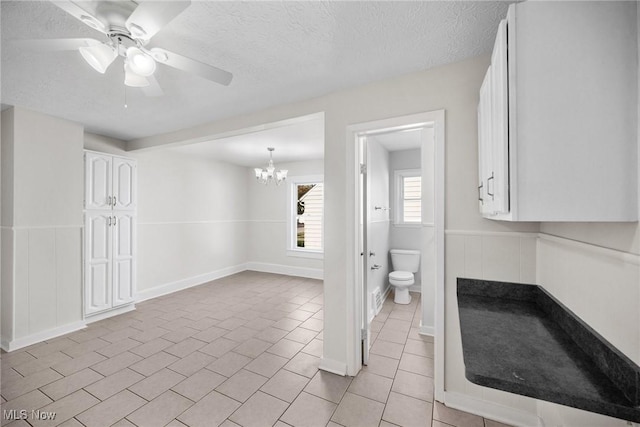 bathroom with ceiling fan with notable chandelier, tile patterned floors, a textured ceiling, and toilet