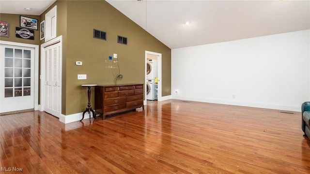 living room with hardwood / wood-style floors, high vaulted ceiling, and stacked washer and clothes dryer