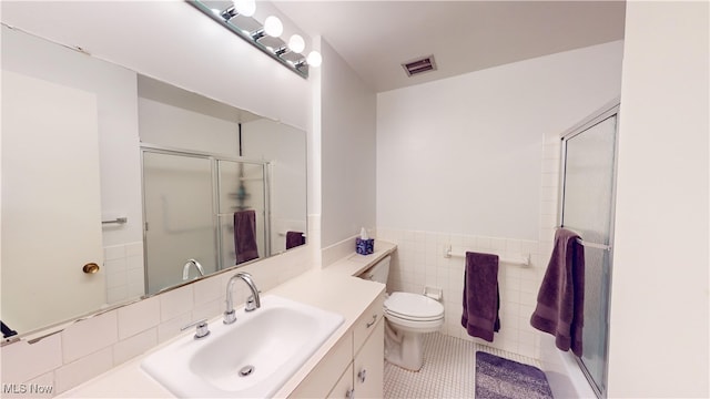 bathroom with vanity, a shower with door, tile walls, tile patterned flooring, and toilet