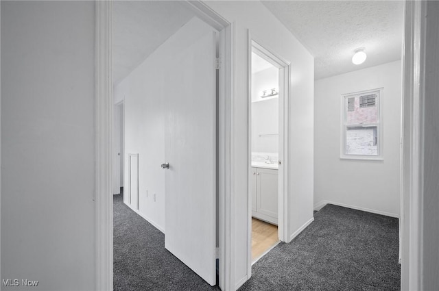 hallway featuring dark carpet and a textured ceiling