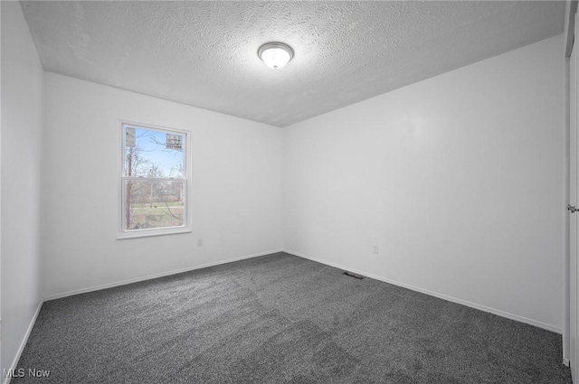 spare room featuring dark carpet and a textured ceiling