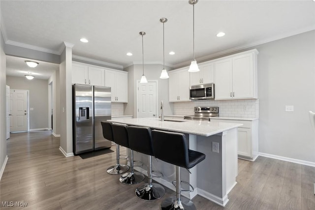 kitchen featuring appliances with stainless steel finishes, a center island with sink, white cabinetry, and decorative light fixtures