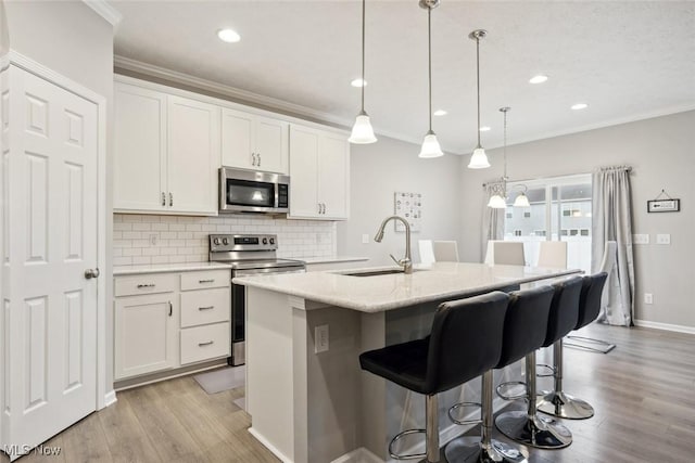 kitchen with decorative light fixtures, stainless steel appliances, white cabinetry, a sink, and an island with sink