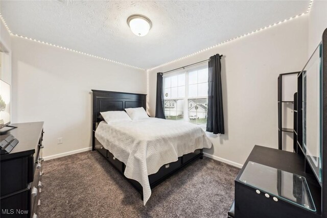 bedroom with a textured ceiling, dark carpet, and baseboards