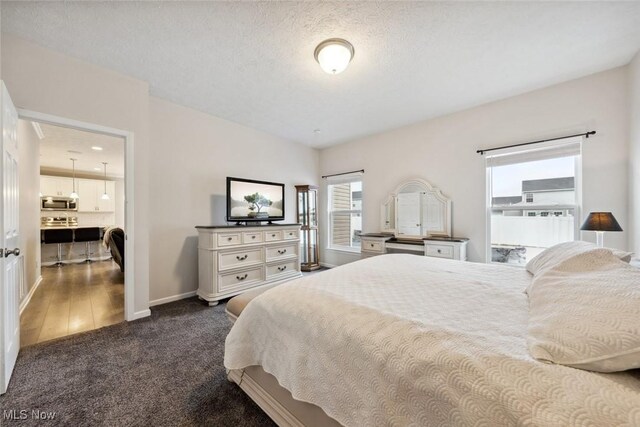 bedroom with a textured ceiling, dark carpet, and baseboards