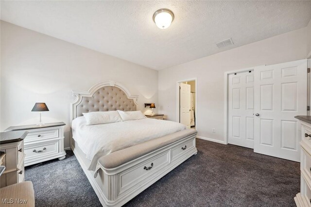 bedroom with a textured ceiling, dark carpet, visible vents, and baseboards