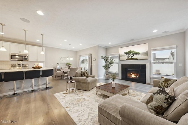 living room featuring light wood finished floors, recessed lighting, ornamental molding, and a tile fireplace