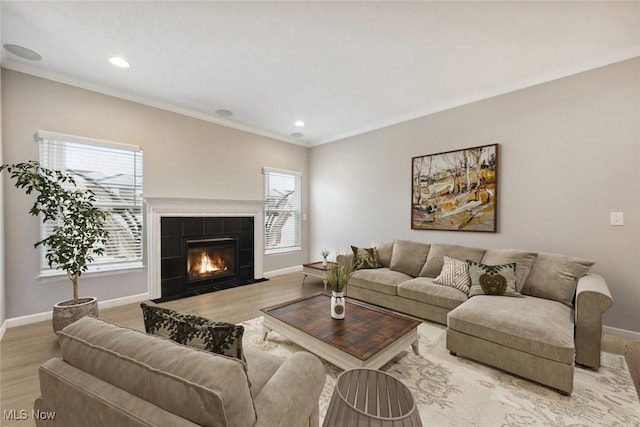 living room with crown molding, light wood finished floors, a tiled fireplace, and baseboards