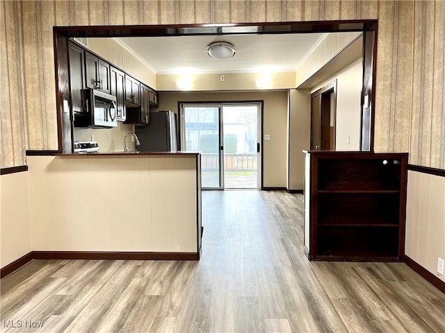 kitchen with kitchen peninsula, stainless steel appliances, light hardwood / wood-style flooring, and ornamental molding